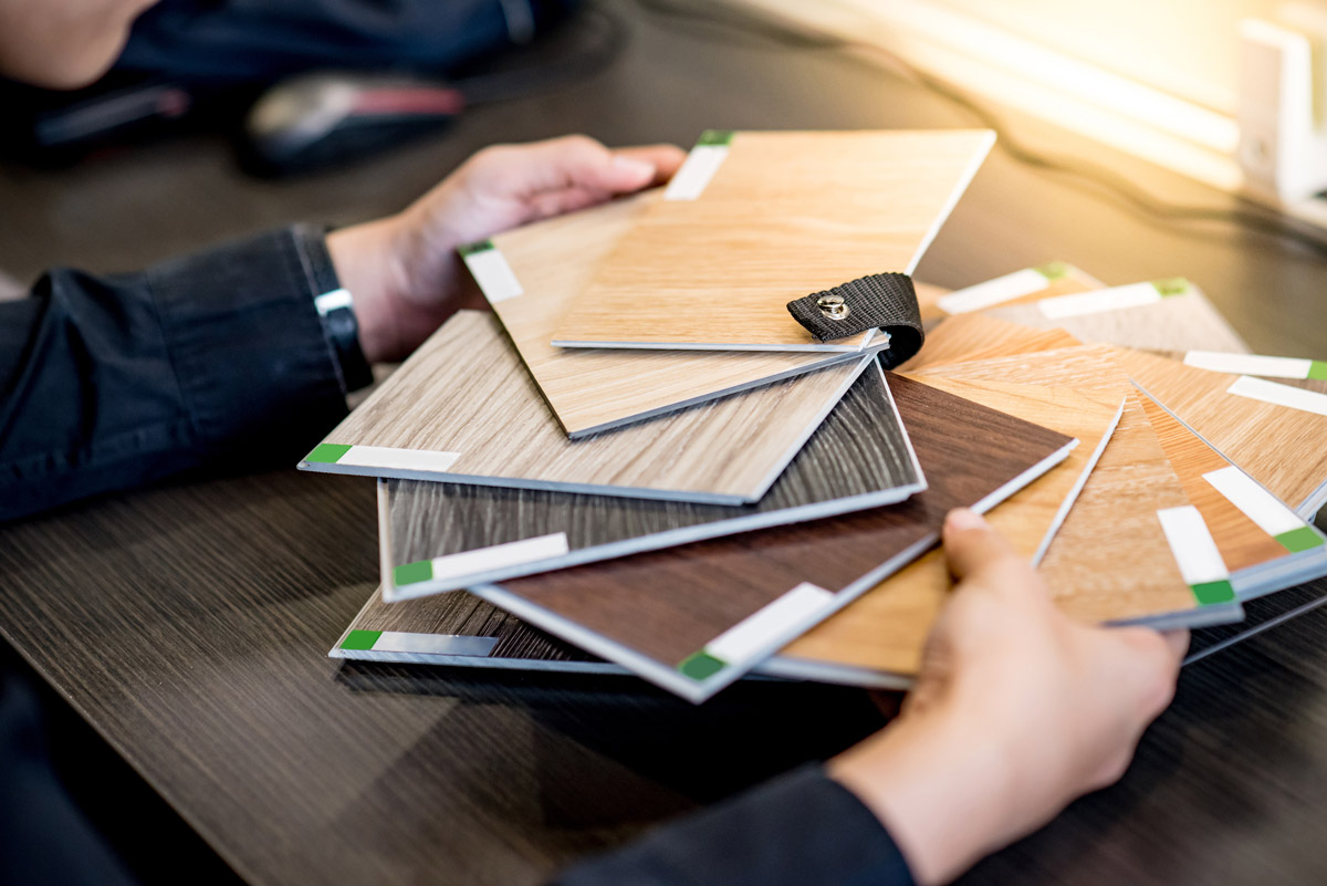 An unseen person holds a swatch book of hardwood flooring.