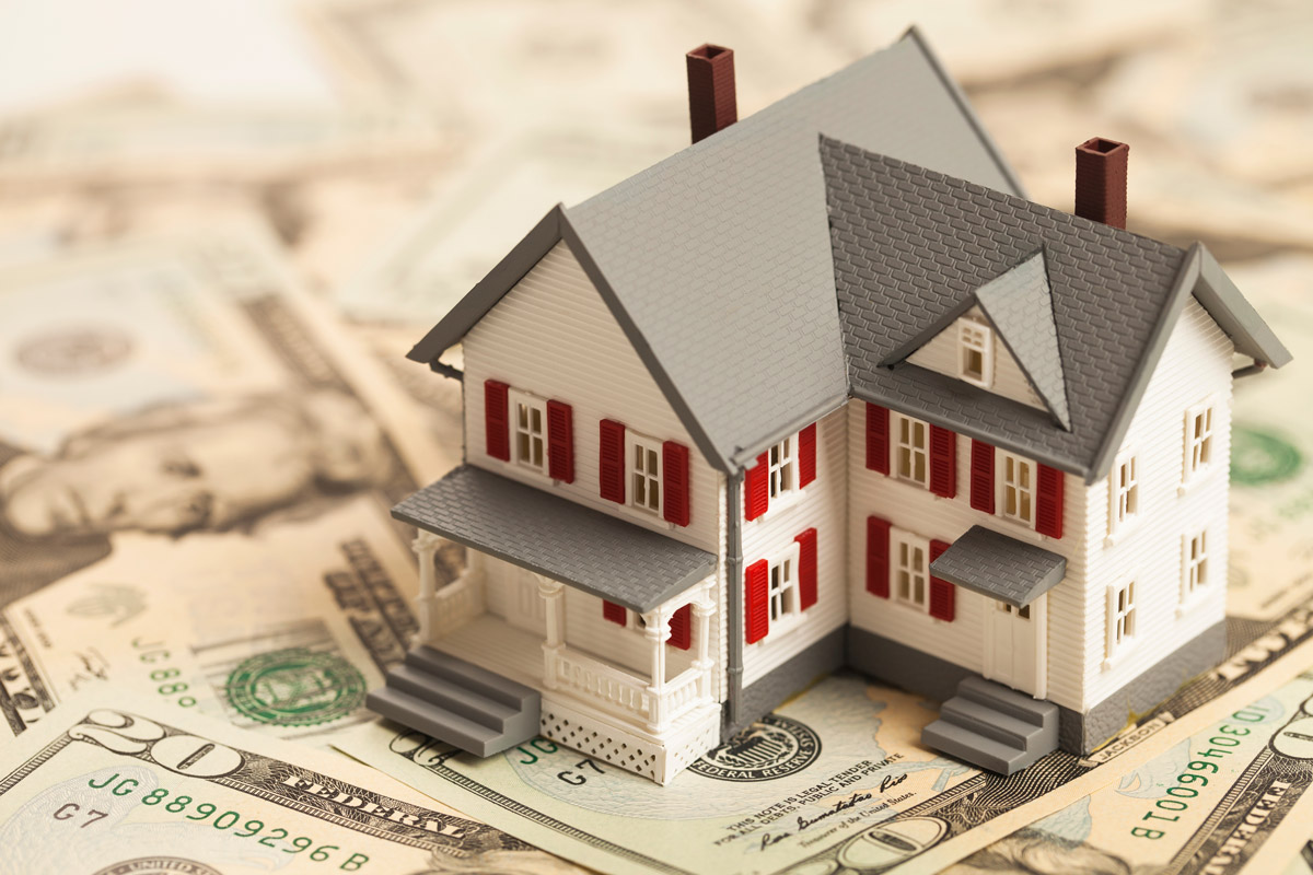 A small model house sits on a pile of money.
